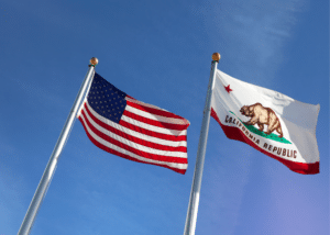 An American flag waving alongside a state of California flag against a blue sky