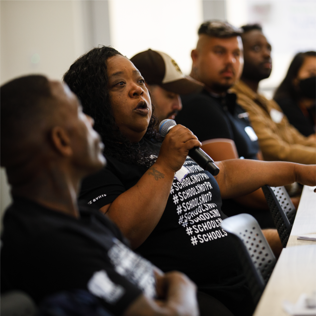 Mid-age woman of color sitting on a panel and speaking to a microphone